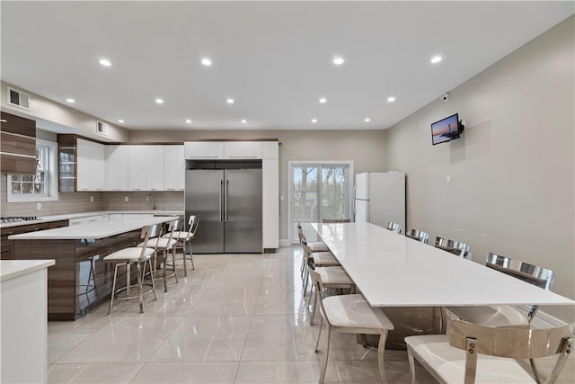 kitchen with a kitchen bar, backsplash, stainless steel appliances, white cabinets, and a kitchen island