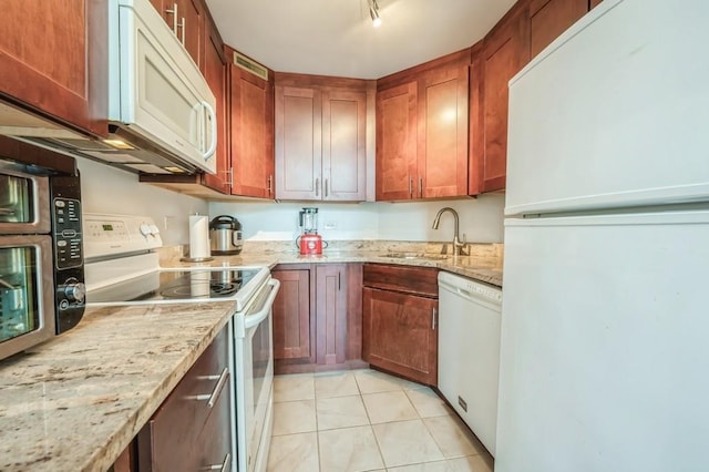 kitchen with light tile patterned floors, white appliances, light stone counters, and sink