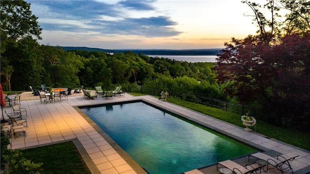 pool at dusk featuring a patio area and a water view