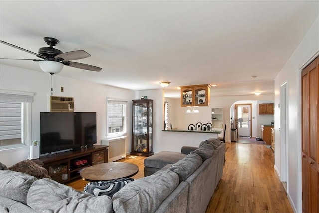 living room featuring a wall unit AC, ceiling fan, radiator heating unit, and light wood-type flooring