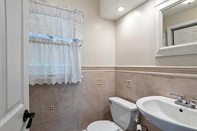 bathroom featuring toilet, tile walls, and sink