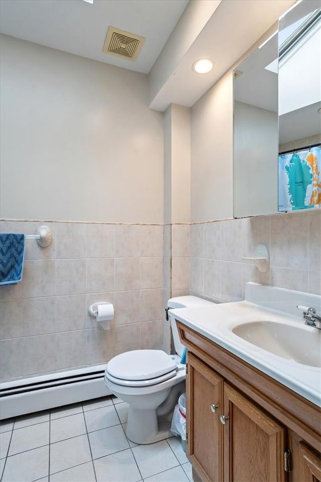 bathroom with a baseboard heating unit, tile patterned floors, toilet, vanity, and tile walls