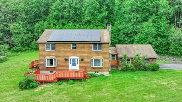 view of front of property with a wooden deck, a front lawn, and solar panels