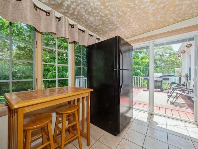 kitchen featuring a kitchen bar, black refrigerator, and light tile patterned floors