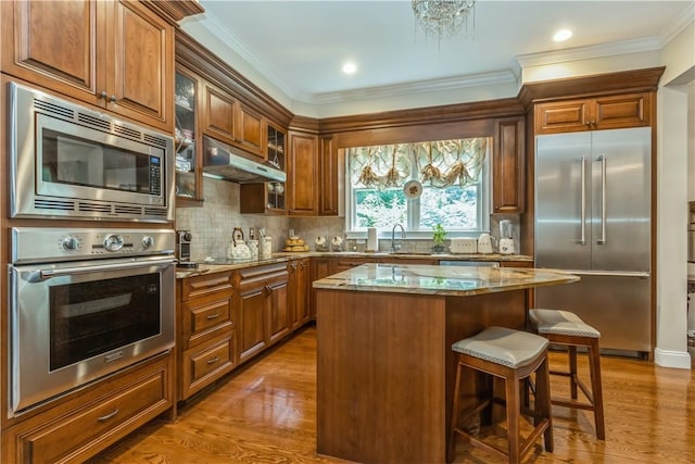 kitchen with built in appliances, light stone countertops, hardwood / wood-style floors, and a kitchen island