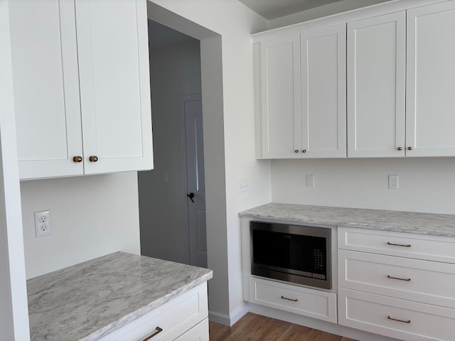 kitchen with white cabinetry, built in microwave, hardwood / wood-style floors, and light stone countertops