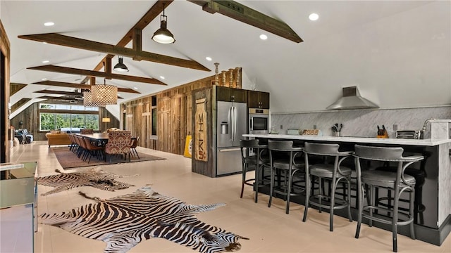 kitchen with beam ceiling, wall chimney exhaust hood, stainless steel appliances, tasteful backsplash, and a breakfast bar area