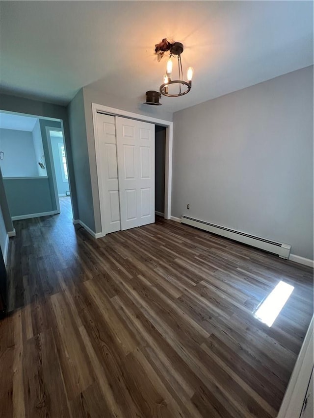 unfurnished bedroom with a closet, dark wood-type flooring, a baseboard radiator, and an inviting chandelier