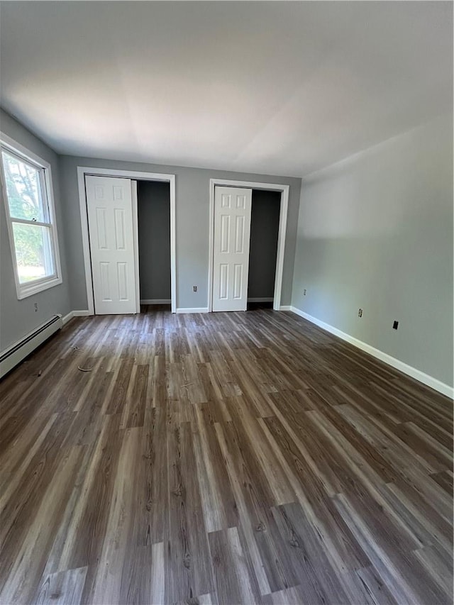 unfurnished bedroom with baseboard heating, multiple closets, and dark hardwood / wood-style flooring