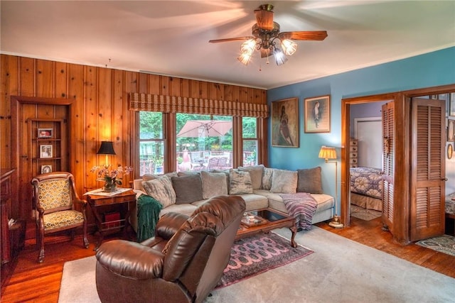 living room featuring hardwood / wood-style flooring, ceiling fan, and wooden walls