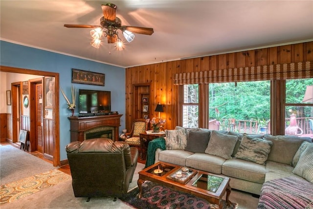 living room with carpet floors, wood walls, ceiling fan, and ornamental molding