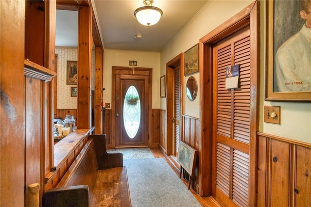 doorway with wood walls, crown molding, and light carpet