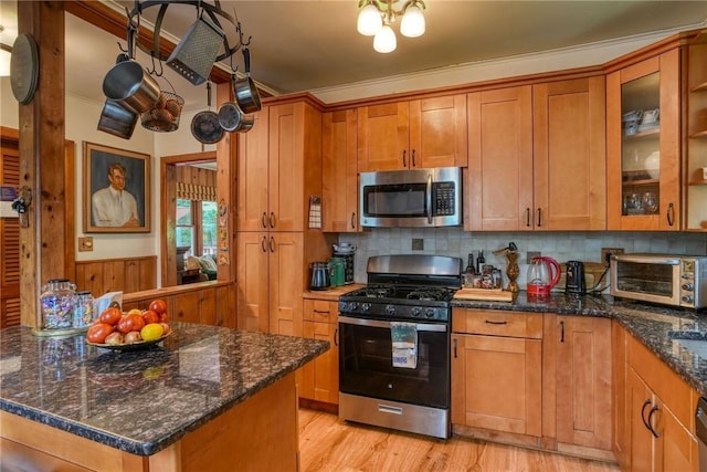 kitchen with backsplash, dark stone counters, light hardwood / wood-style flooring, ornamental molding, and stainless steel appliances