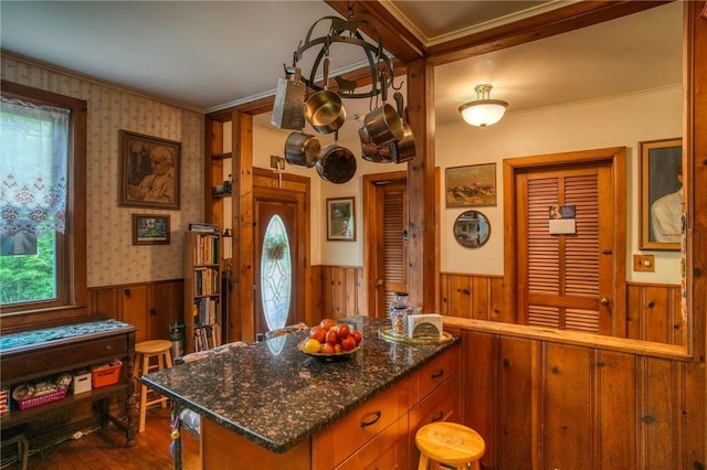 kitchen featuring dark hardwood / wood-style flooring, dark stone counters, ornamental molding, a kitchen island, and wood walls