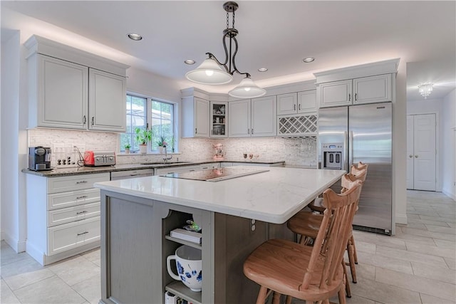 kitchen featuring stainless steel refrigerator with ice dispenser, black electric stovetop, decorative light fixtures, a kitchen island, and light stone counters