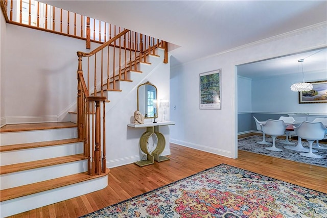 stairway with a chandelier, ornamental molding, and hardwood / wood-style floors