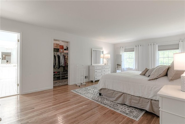 bedroom with a closet, a walk in closet, light hardwood / wood-style floors, and ensuite bath