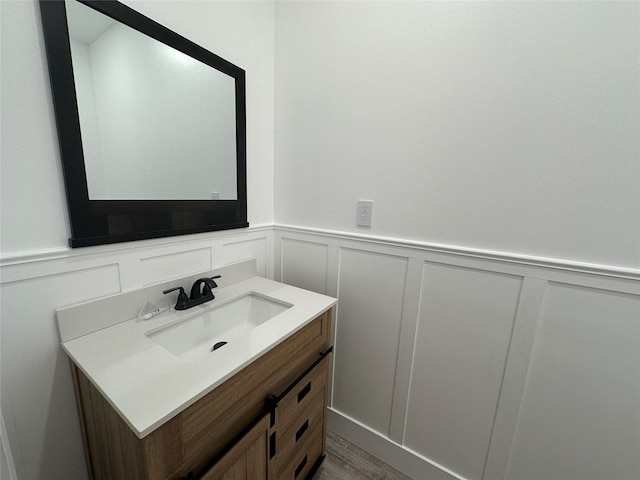 bathroom featuring wainscoting, a decorative wall, vanity, and wood finished floors