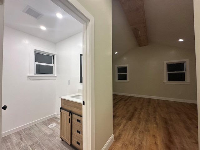 interior space with light wood-style floors, visible vents, vaulted ceiling with beams, and baseboards