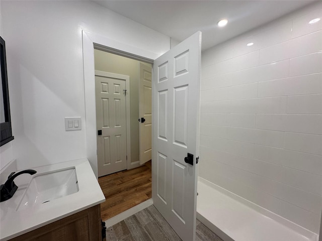 bathroom featuring a tile shower, vanity, wood finished floors, and recessed lighting