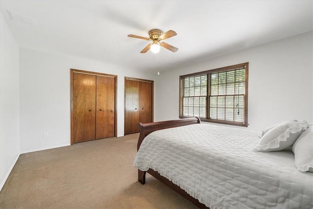 carpeted bedroom with ceiling fan and multiple closets