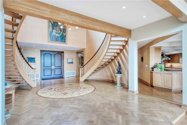 entryway featuring a towering ceiling, beamed ceiling, and light parquet flooring