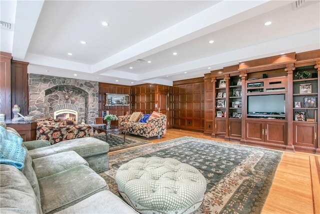 living room with beam ceiling, hardwood / wood-style floors, a stone fireplace, and built in features