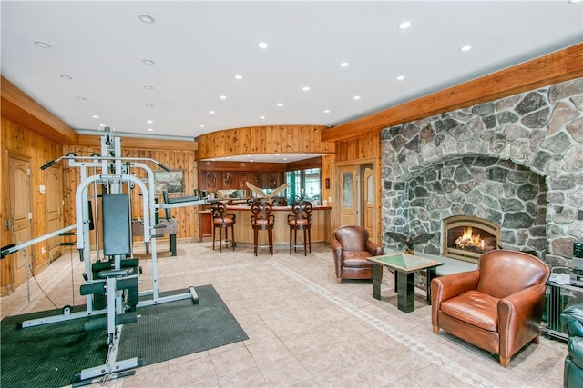 exercise room with light tile patterned floors, a stone fireplace, and wood walls