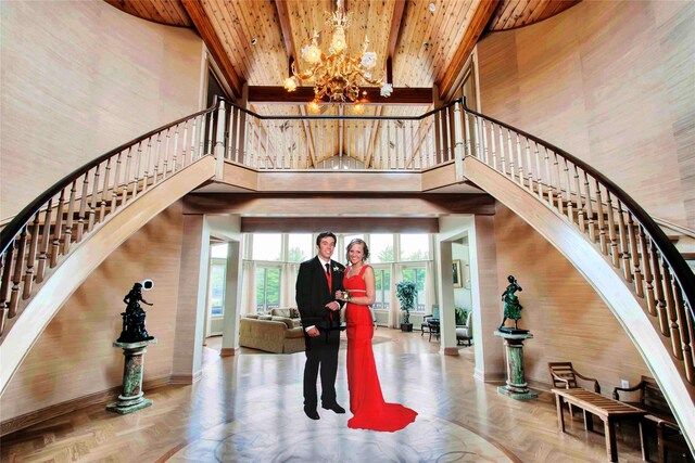 stairway with a notable chandelier, a towering ceiling, parquet floors, and wooden ceiling