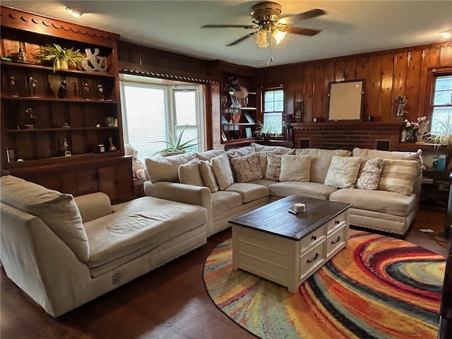 living room with ceiling fan, wooden walls, and dark wood-type flooring