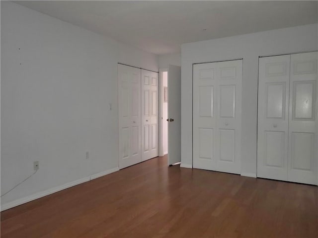 unfurnished bedroom featuring dark hardwood / wood-style floors and two closets