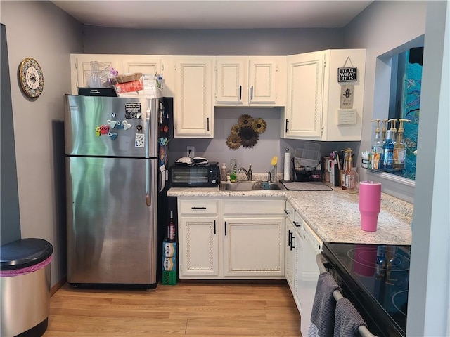 kitchen featuring white cabinets, light wood-type flooring, stainless steel refrigerator, and black / electric stove