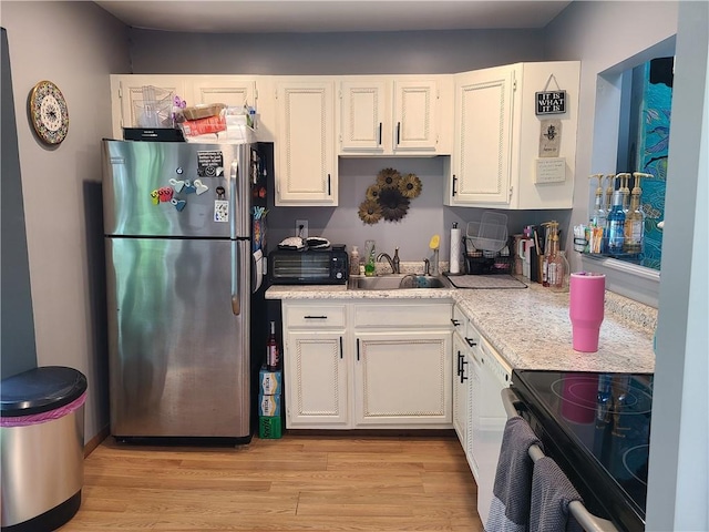 kitchen featuring black electric range oven, sink, light wood-type flooring, white cabinetry, and stainless steel refrigerator