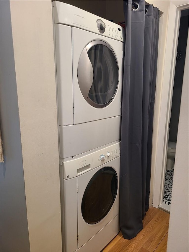 clothes washing area with light wood-type flooring and stacked washer and clothes dryer