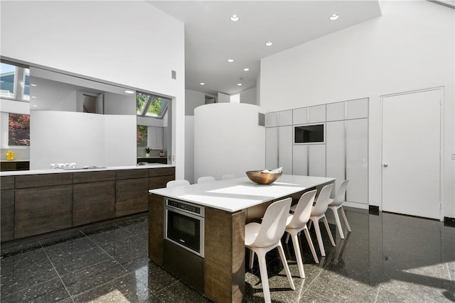 kitchen with oven, a kitchen island, a towering ceiling, and a breakfast bar area