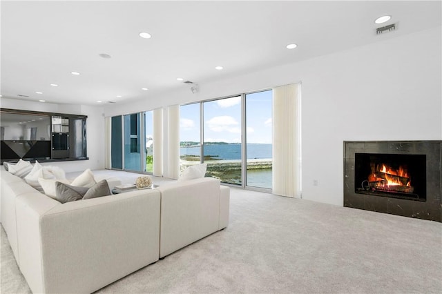 living room with light carpet, a water view, and a tiled fireplace