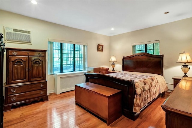 bedroom featuring a wall unit AC, multiple windows, radiator, and light wood-type flooring