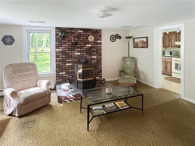 sitting room with carpet flooring, a wood stove, ceiling fan, and a baseboard heating unit