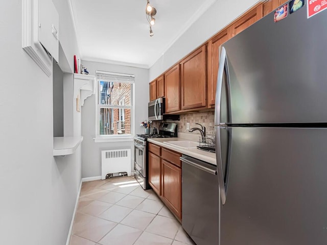 kitchen with sink, radiator heating unit, backsplash, light tile patterned flooring, and appliances with stainless steel finishes