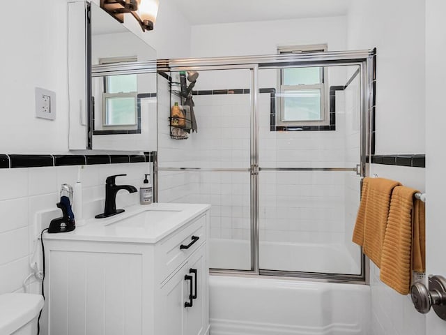 full bathroom featuring combined bath / shower with glass door, vanity, toilet, and tile walls