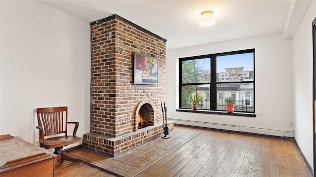 living room with baseboard heating, a fireplace, and wood-type flooring