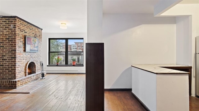 unfurnished living room featuring dark wood-type flooring, a brick fireplace, and a baseboard heating unit