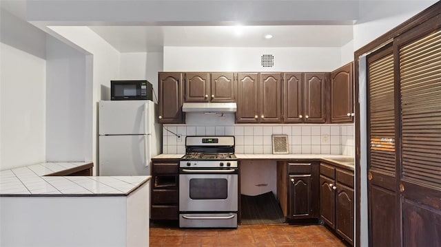 kitchen with white refrigerator, tasteful backsplash, dark brown cabinetry, and stainless steel gas range