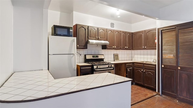 kitchen featuring tile countertops, dark brown cabinets, white fridge, and gas range