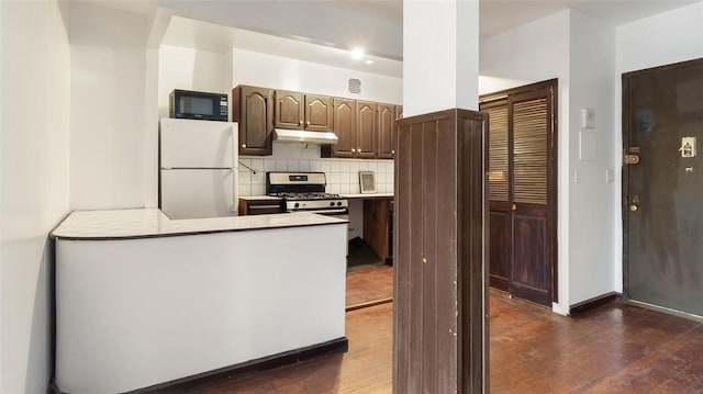 kitchen with gas range, backsplash, white fridge, and dark hardwood / wood-style floors