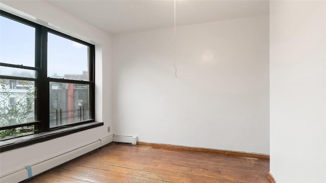 unfurnished room featuring hardwood / wood-style floors and a baseboard heating unit