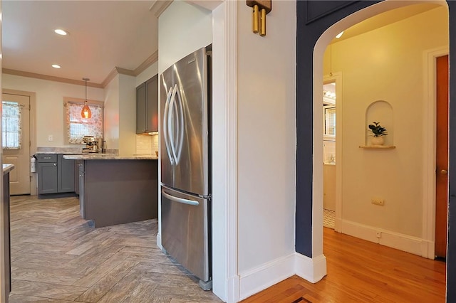 kitchen featuring hanging light fixtures, gray cabinets, stainless steel fridge, ornamental molding, and light stone counters