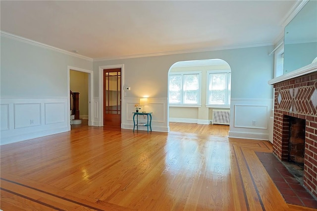 unfurnished living room featuring a fireplace, wood-type flooring, radiator heating unit, and ornamental molding