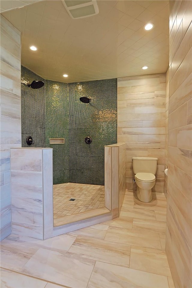 bathroom with tile patterned floors, toilet, tiled shower, and tile walls