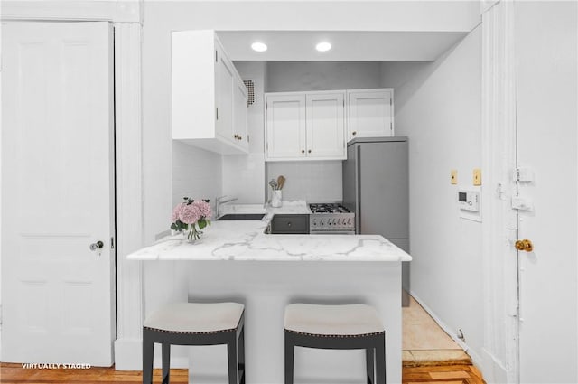 kitchen with white cabinets, a kitchen breakfast bar, sink, light stone countertops, and light wood-type flooring